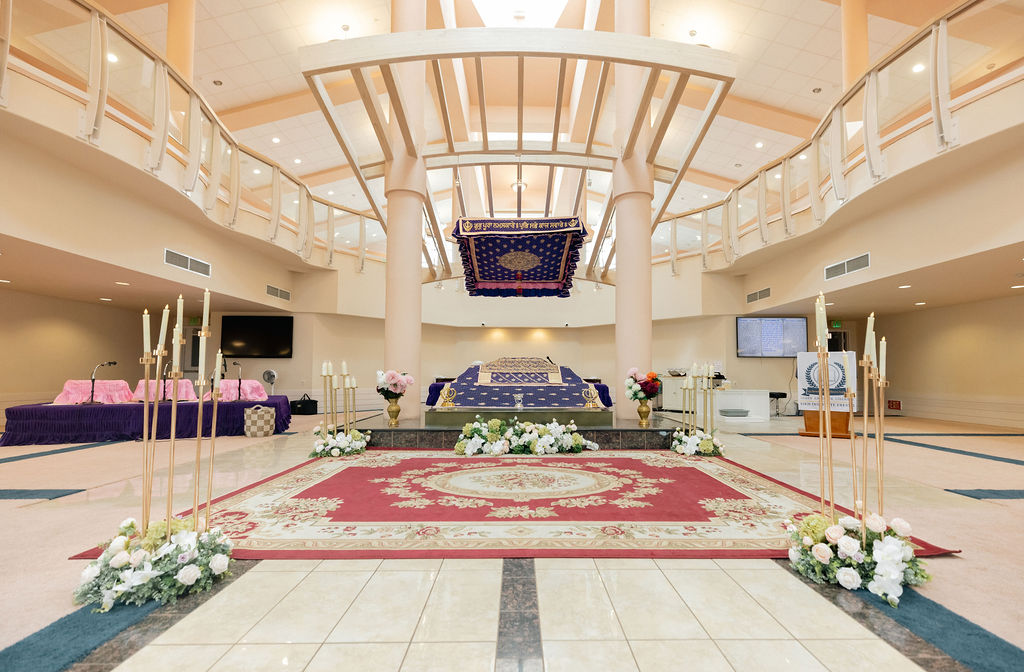 Wide empty Sikh Institute Fresno ceremony hall with white columns, curved balcony, purple canopy, red carpet and wedding flowers