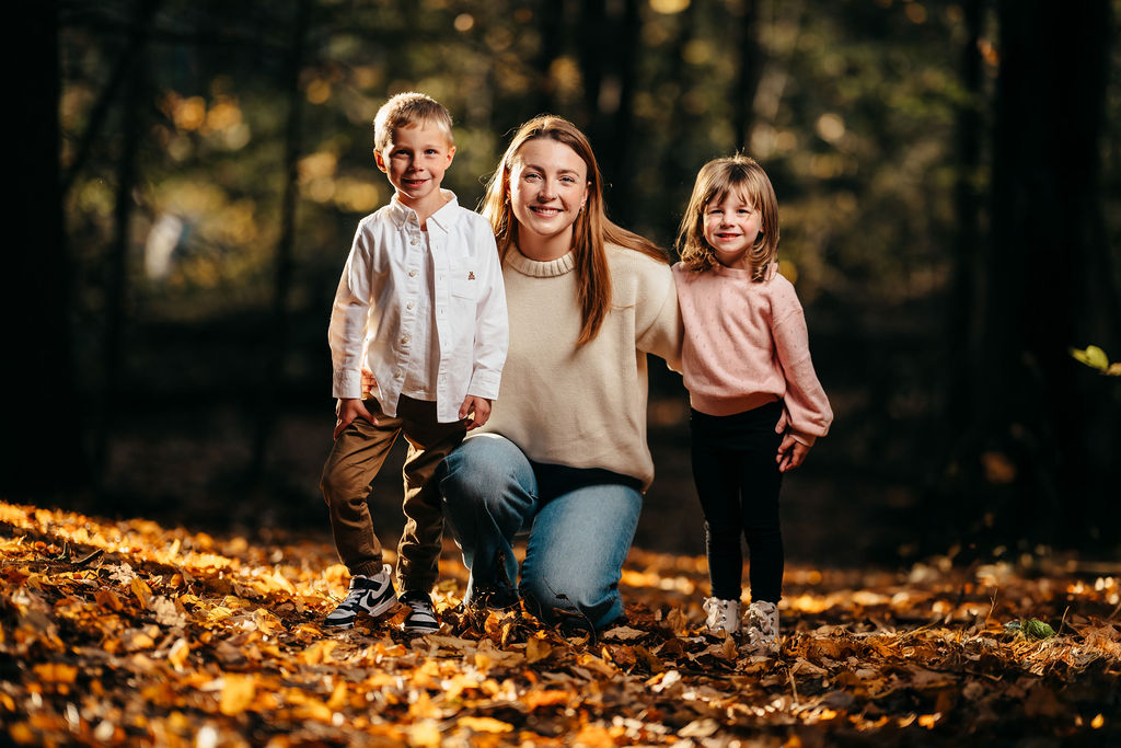 Mother kneeling with her young son and daughter amid golden fallen leaves in the woods