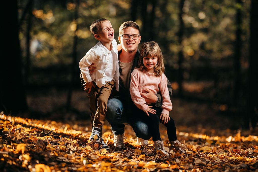 Dad with his laughing son and daughter standing together in the golden leaf-covered woods