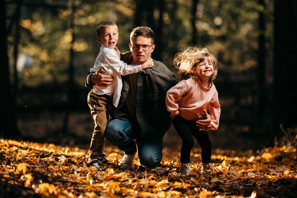 Playful candid of dad with his laughing son and spinning daughter on a bed of golden leaves
