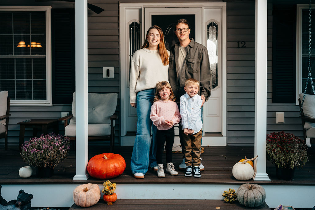 Ekholm family of four on the front porch surrounded by pumpkins and mums