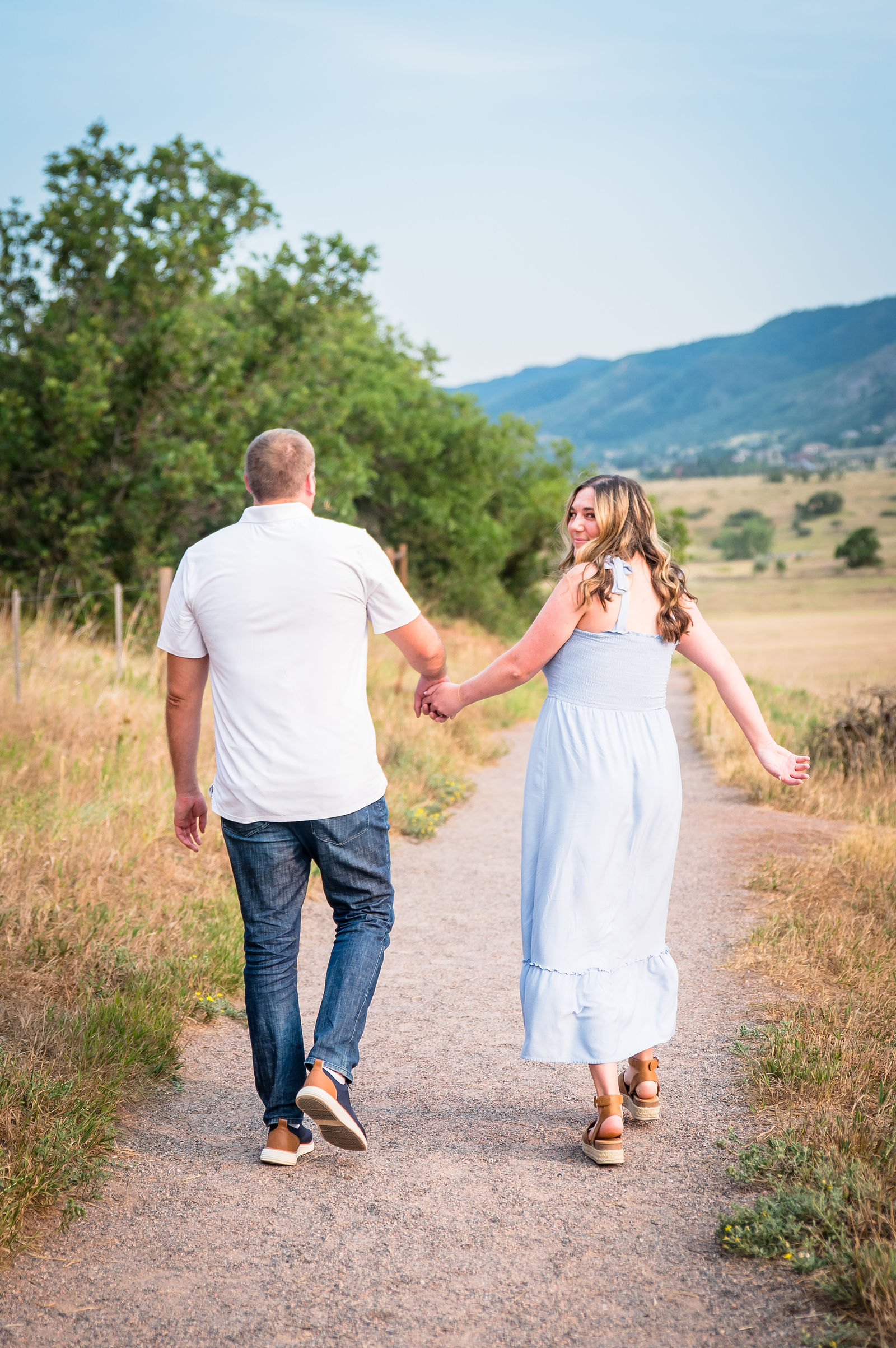 Engaged couple in an open Colorado field with mountains behind them