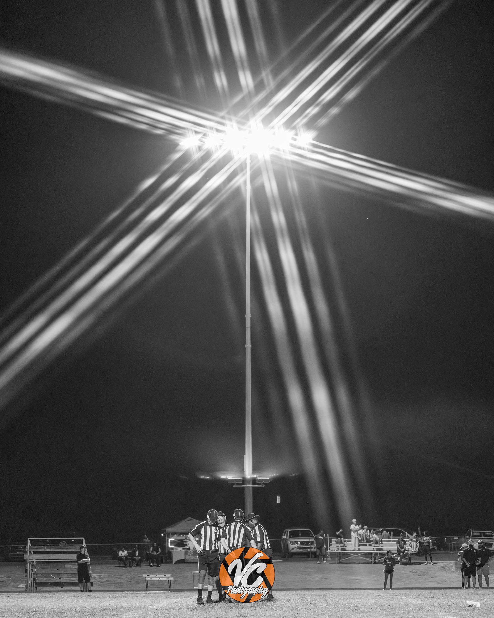 Stadium lights creating dramatic starbursts above officials during the Barton Middle School football game