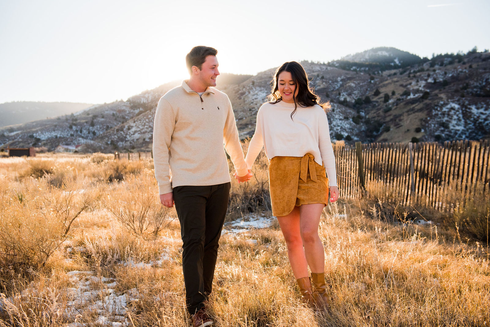 Couple in cream knit sweaters and a camel suede skirt standing in golden late autumn grass in Colorado