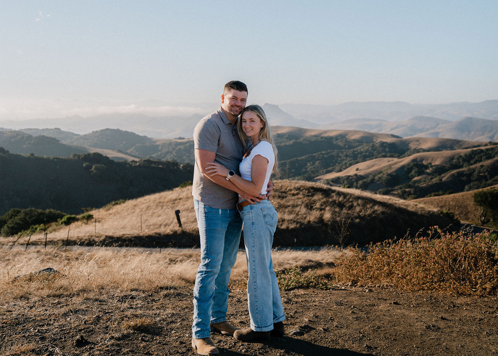 Engaged couple embracing on a golden hillside overlook at sunset, San Luis Obispo Central Coast