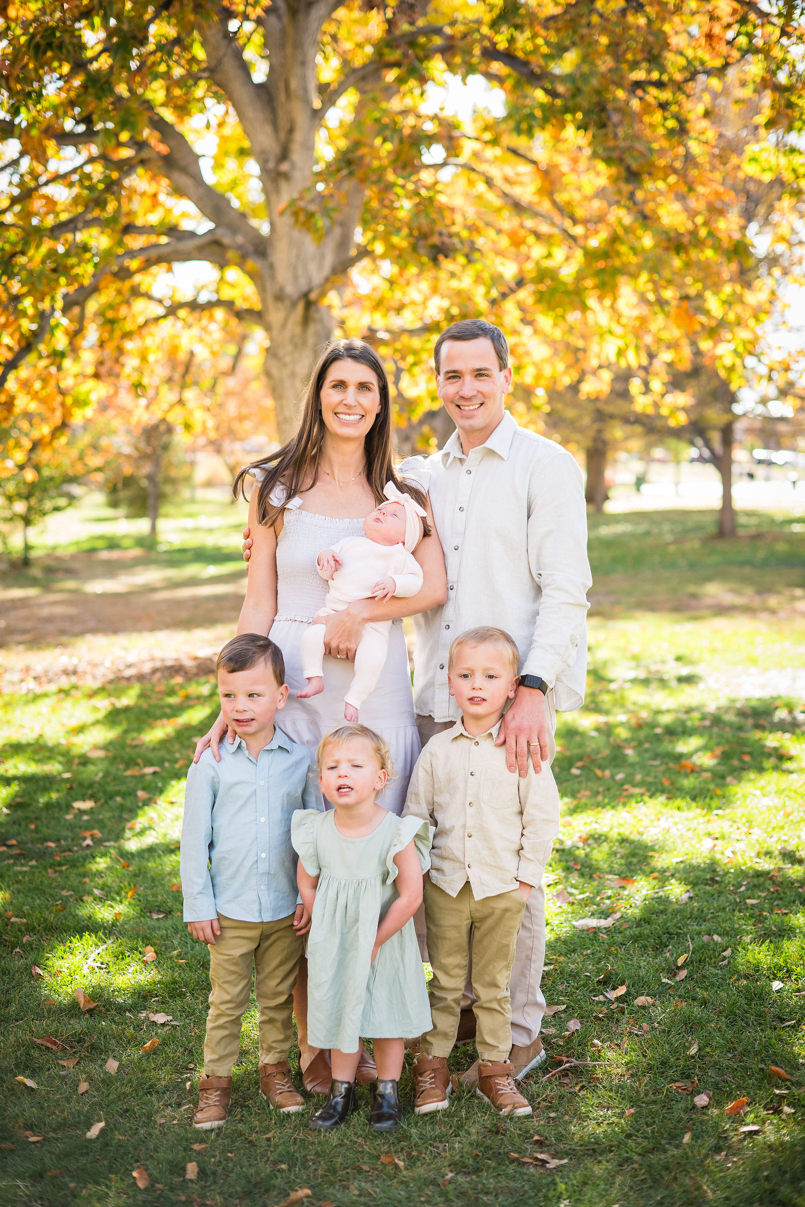 Family of six in cream, khaki and soft blue standing under golden fall trees in Colorado