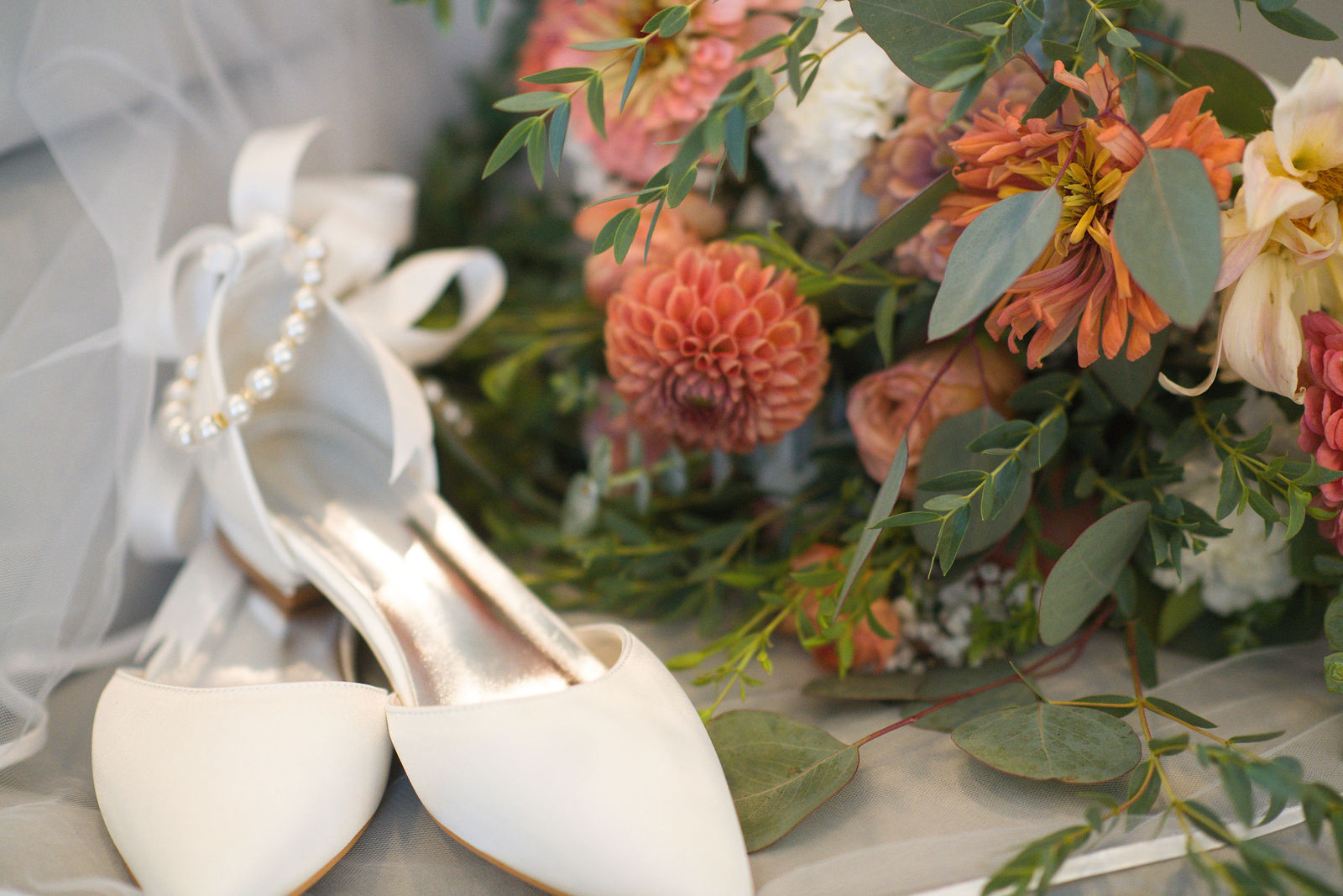 Ivory bridal shoes and pearl details beside a warm floral bouquet