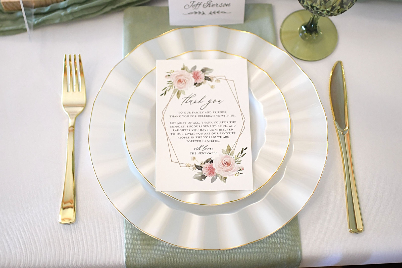 Gold-rimmed wedding place setting with floral stationery and sage linens