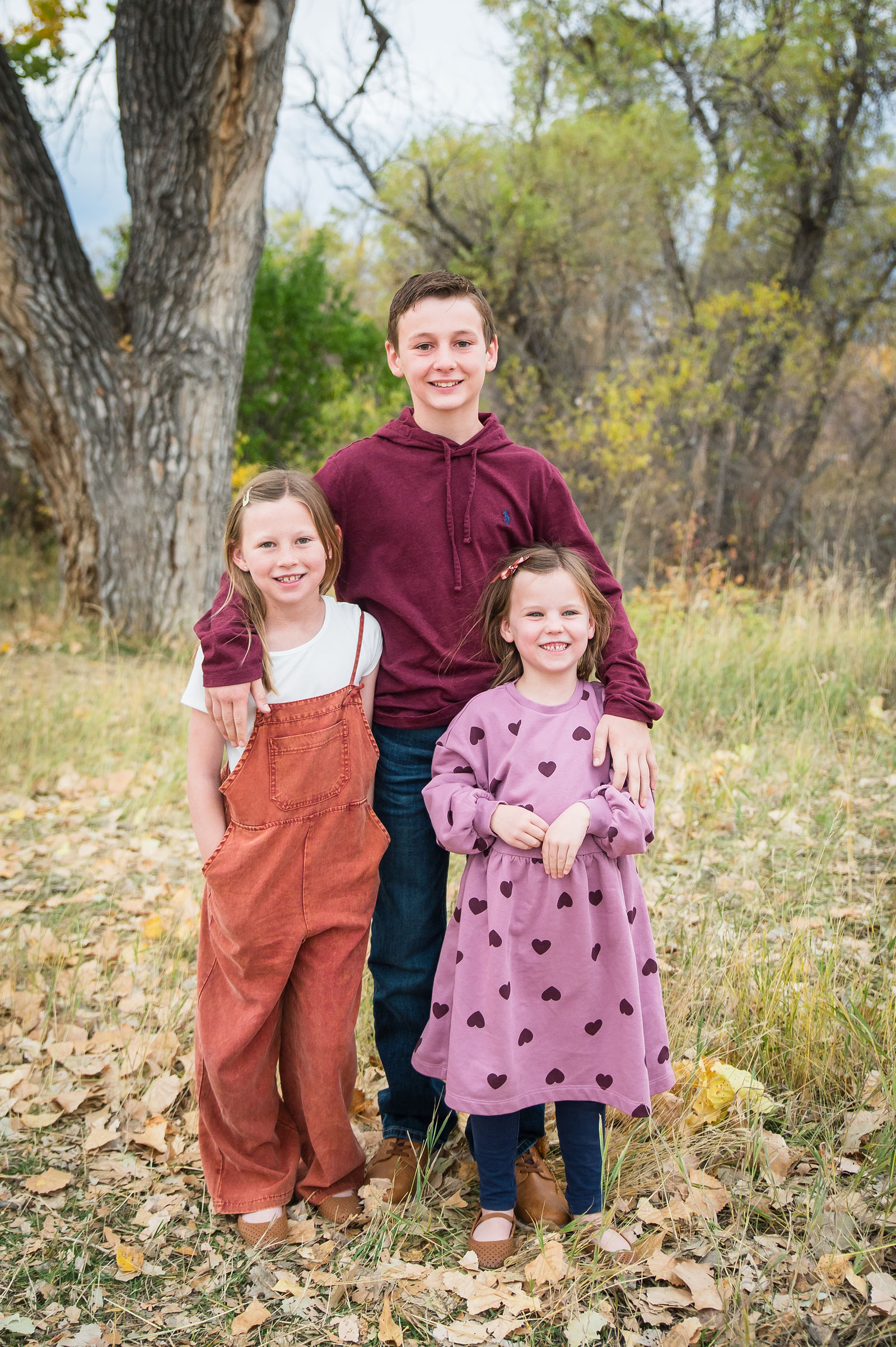 Two sisters in rust and mauve fall outfits standing in front of golden Colorado cottonwoods