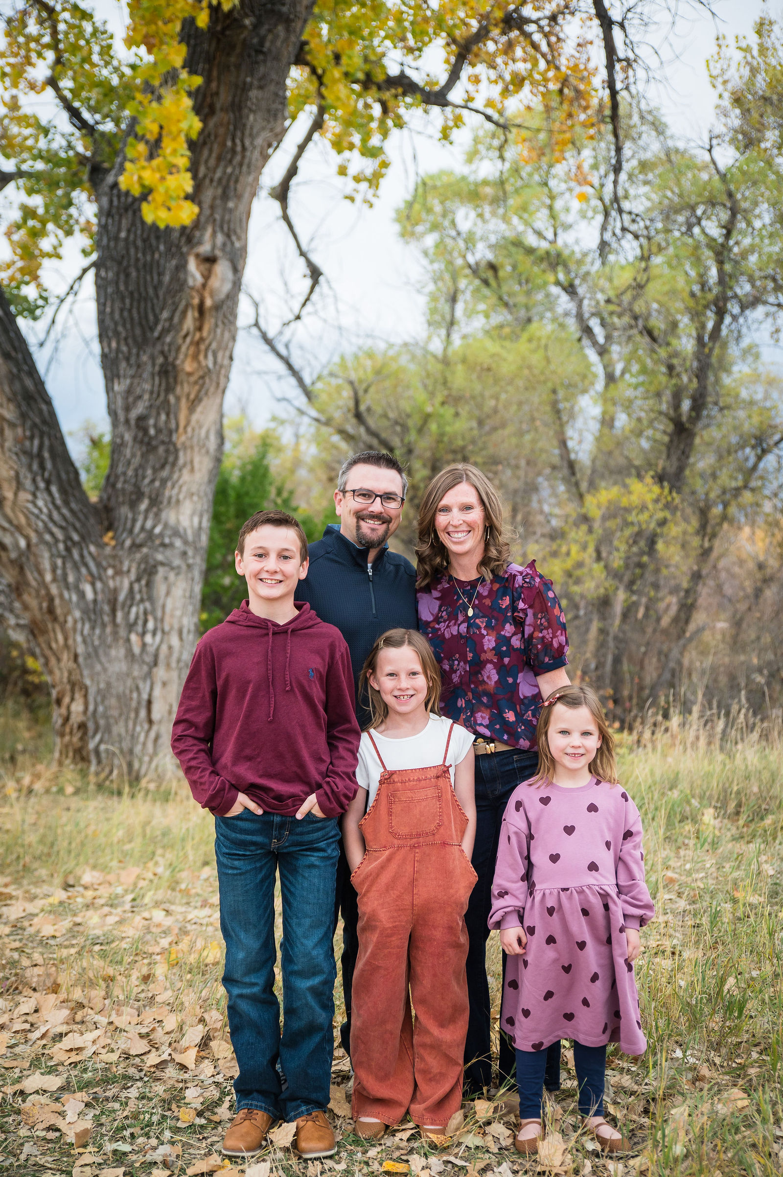 Family in burgundy, rust and navy fall outfits beneath golden Colorado cottonwood trees