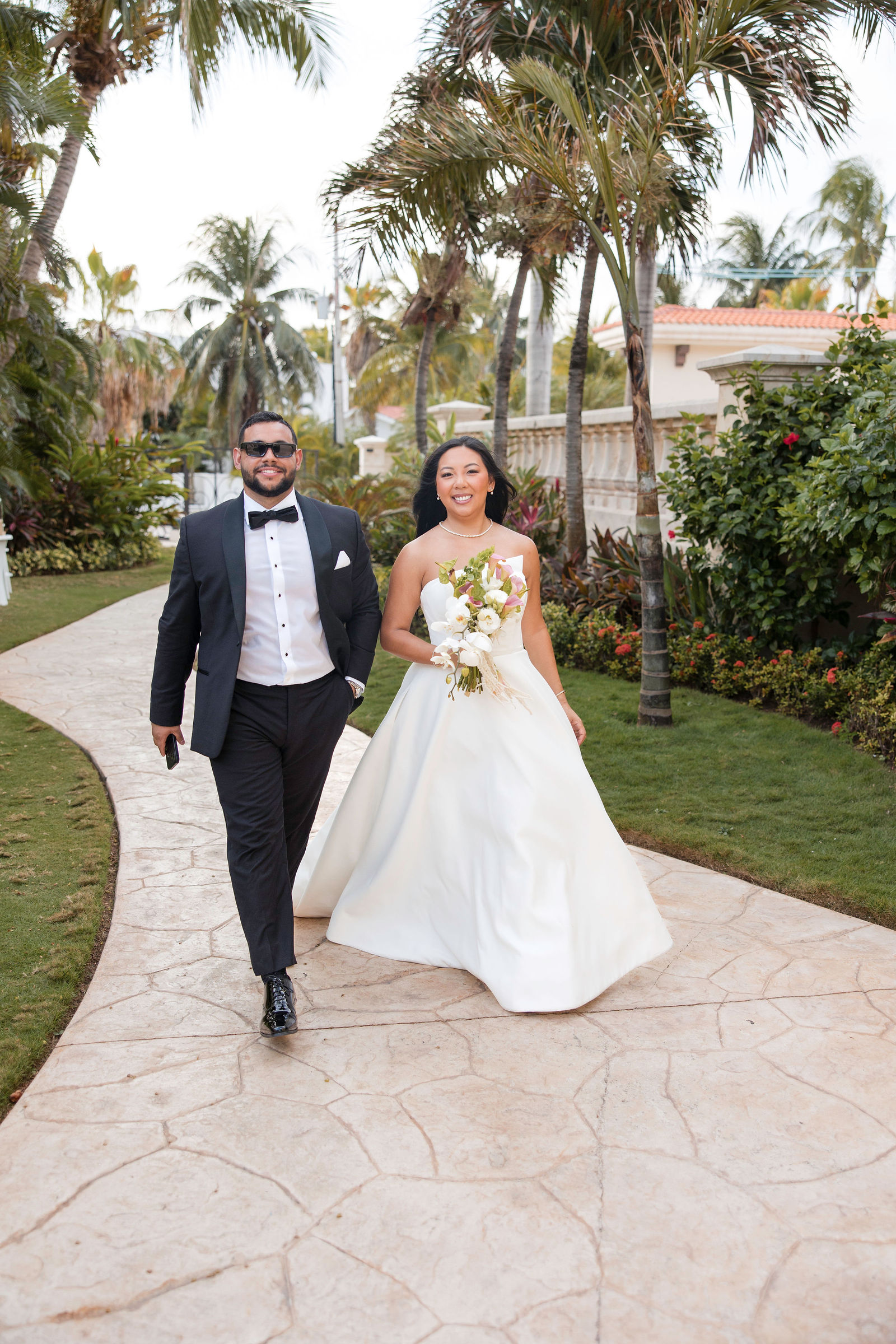 A couple walking a palm-lined garden path after their wedding ceremony, photographed by Arch Wedding Studio