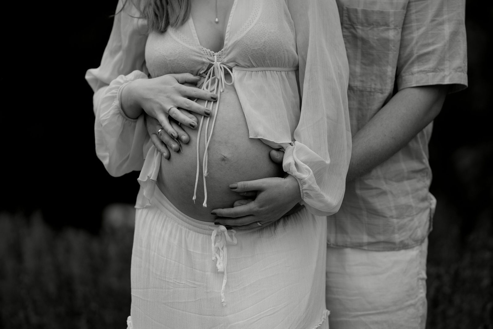 Schwarz-weiße Nahaufnahme eines Babybauchs, liebevoll von beiden Händen der Eltern umfasst, zeitloses Schwangerschaftsfoto