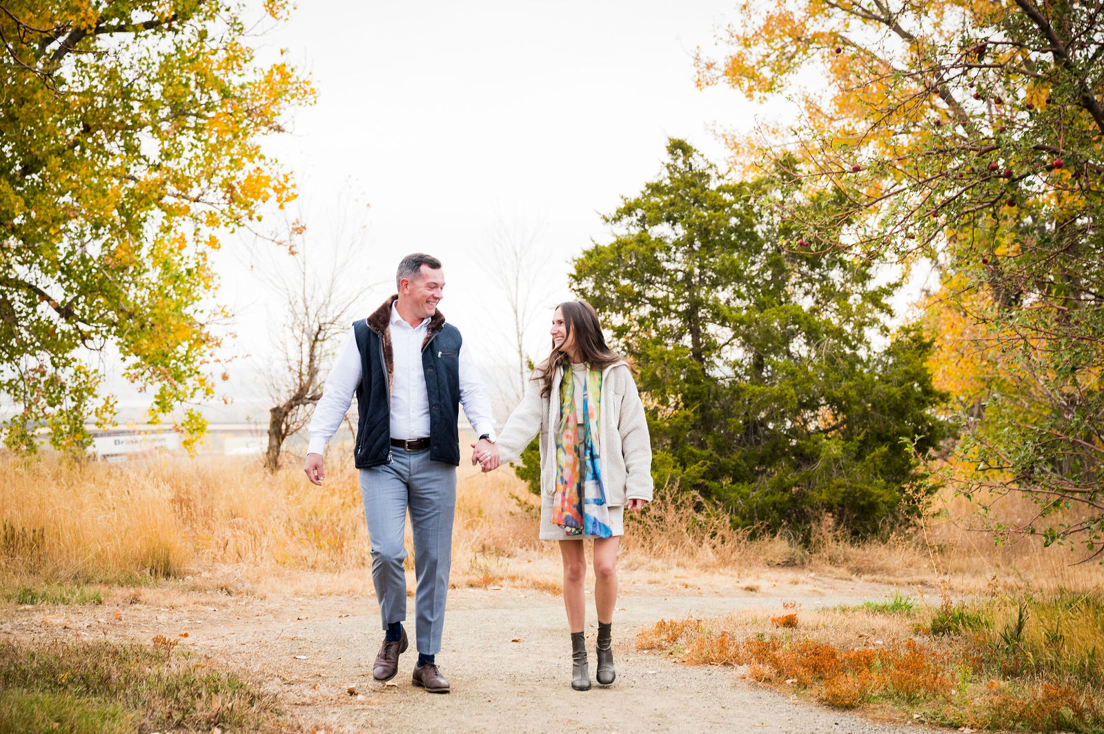 Couple in a navy quilted vest and white button down with a cream cardigan layered over a floral dress in autumn Colorado