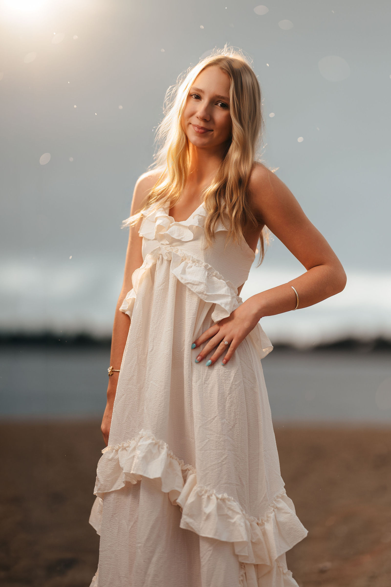 Aly in a white ruffle dress with sun flare by the water during her senior portrait session