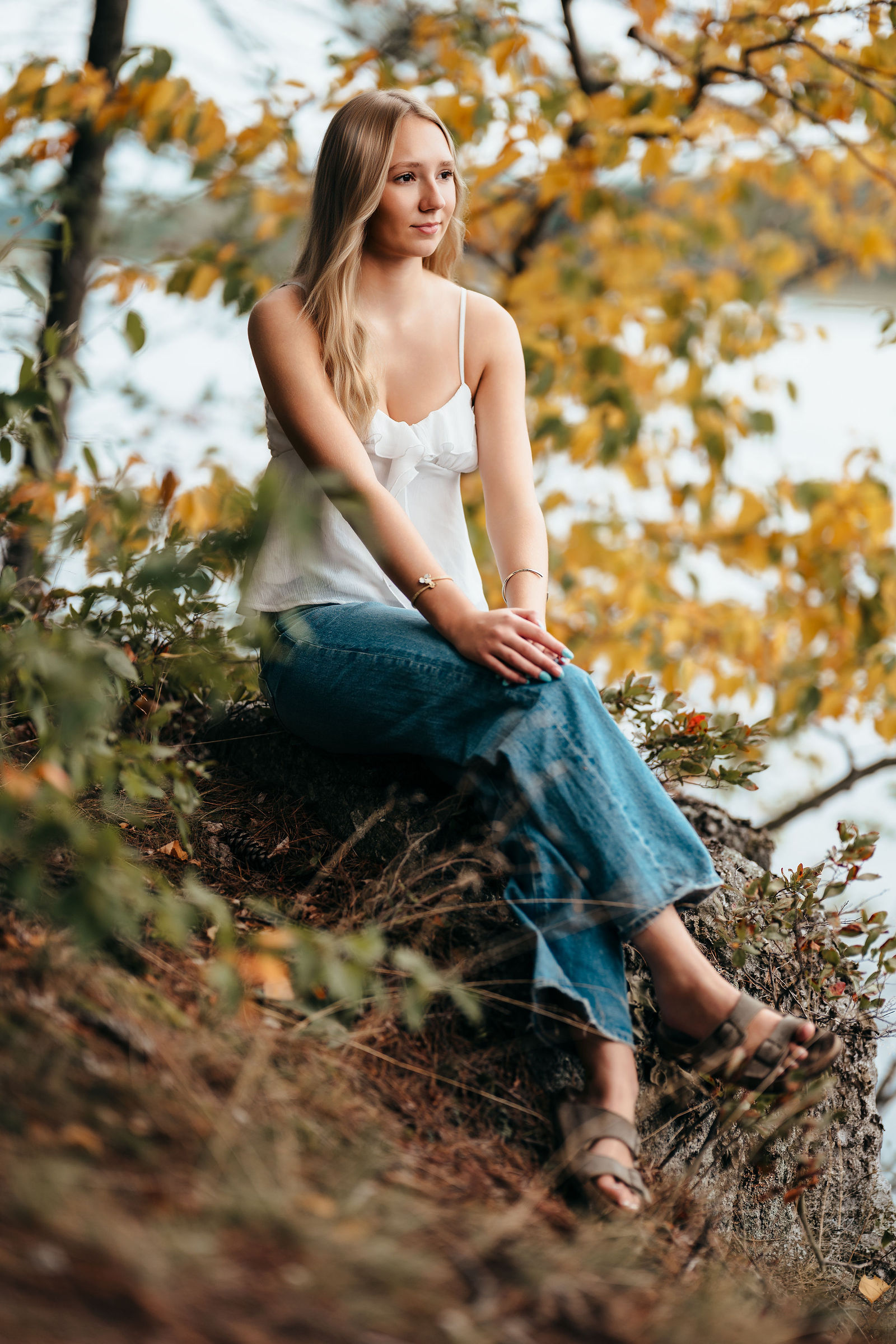 Aly sitting among golden autumn leaves during her senior portrait session
