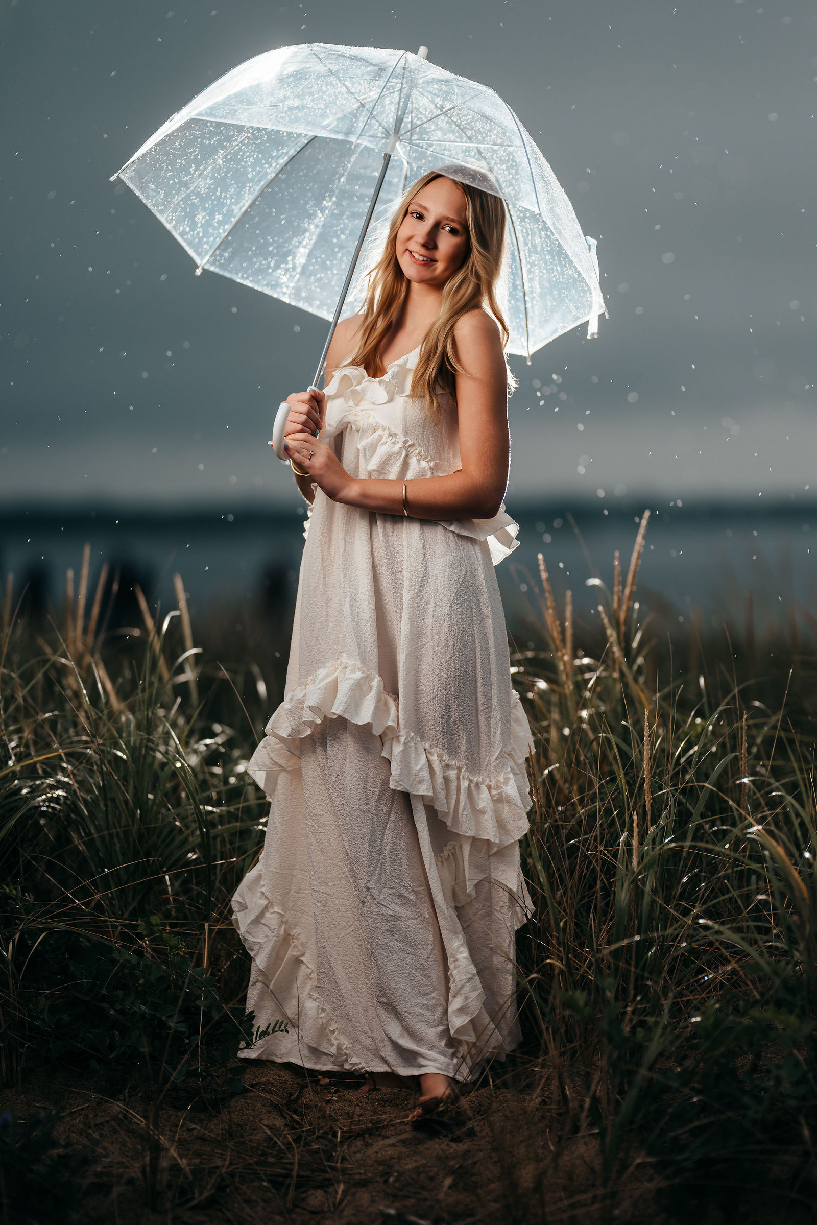 Aly holding a clear umbrella in the rain, backlit, during her senior portrait session