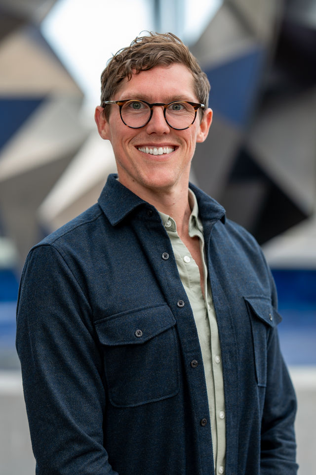 Headshot of a smiling man in glasses and a denim jacket, photographed by Dodi Images
