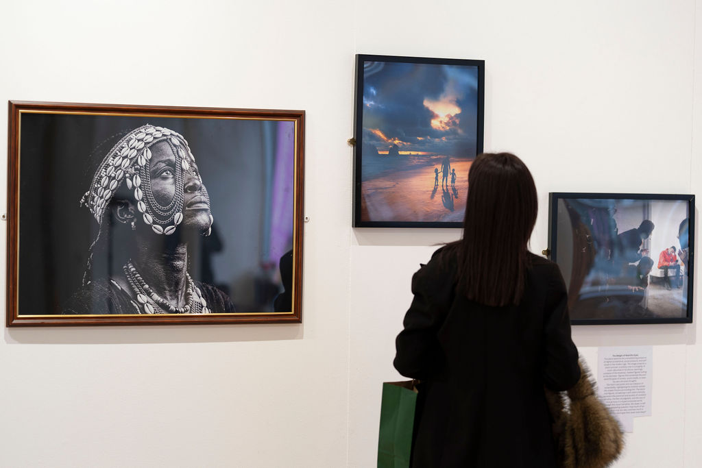 A visitor looking at a framed black and white portrait in a wooden frame next to a framed sunset photograph