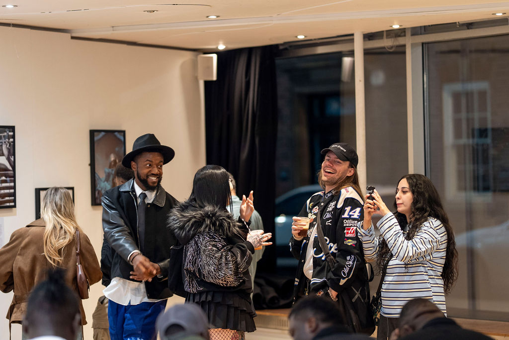 A crowd of guests gathered near the window of the gallery with several people holding up their phones to take photographs
