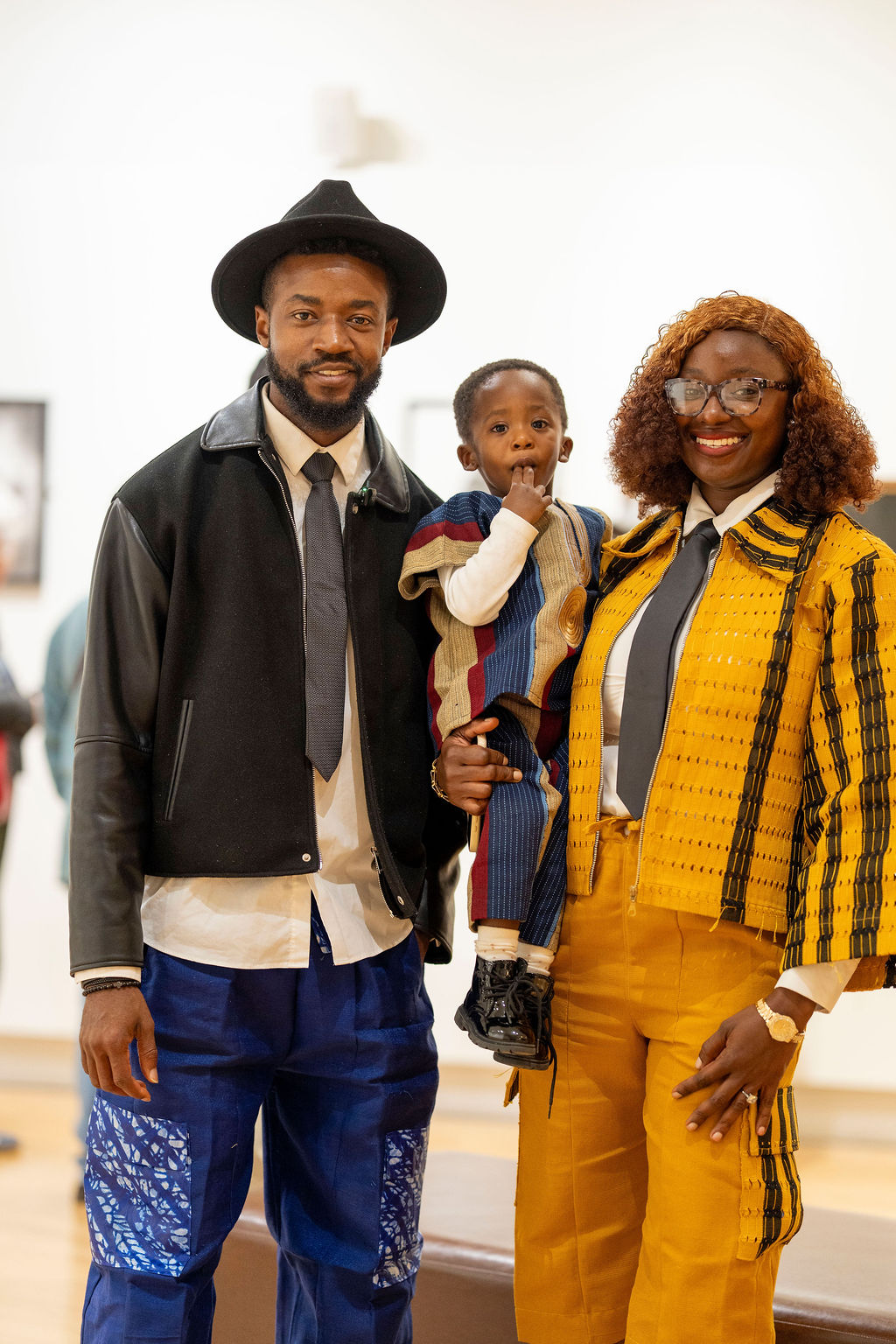 John Lekan holding a young child in the gallery beside a woman in a yellow striped outfit