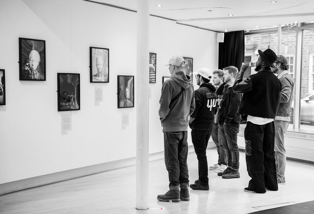 A black and white image of a group of visitors standing together in front of the gallery wall