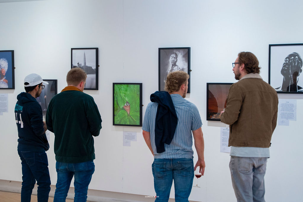 Four visitors in conversation in front of framed photographs on the gallery wall