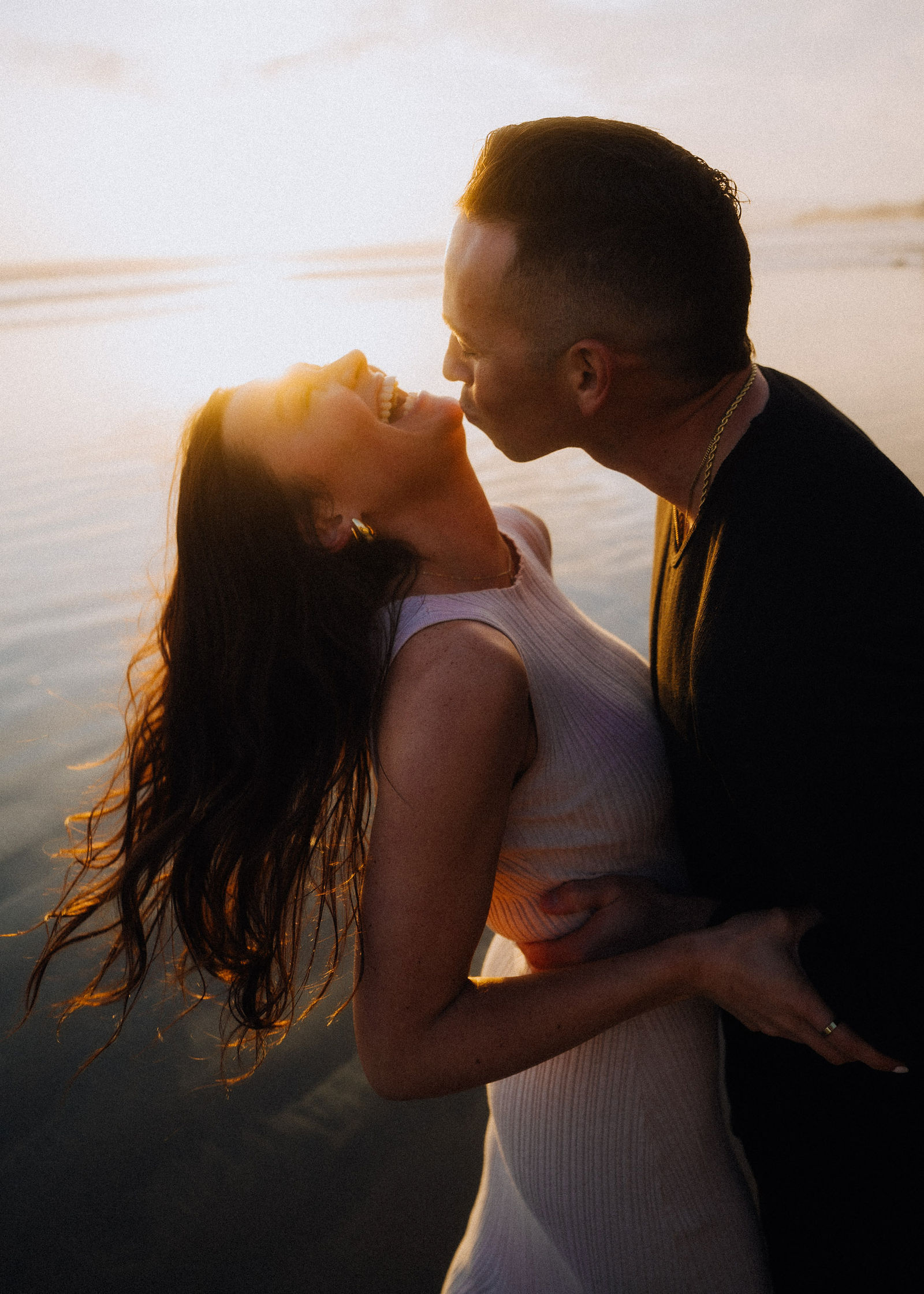A couple caught in a sunlit kiss along the coast.