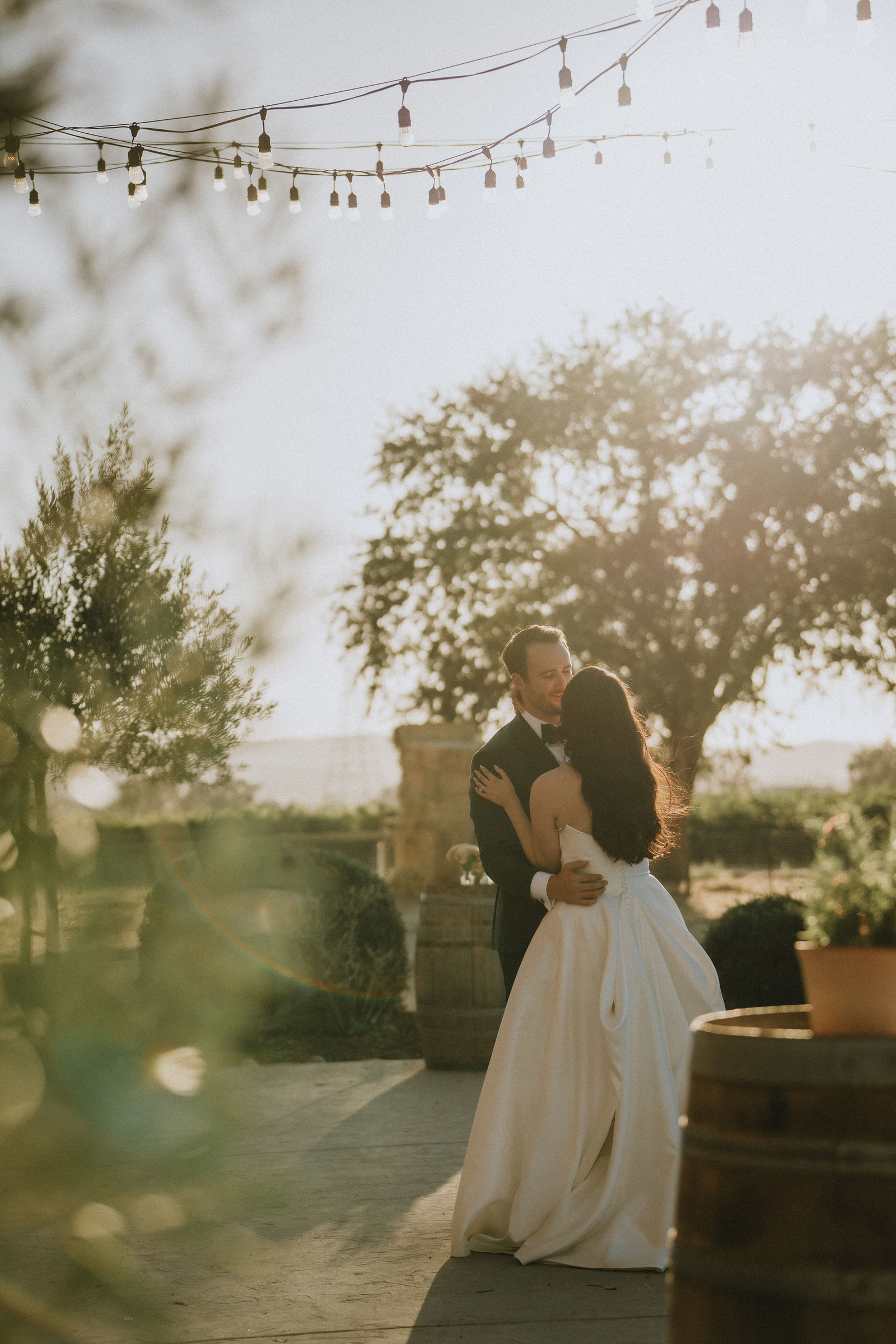 A couple holding each other during their first dance beneath string lights.