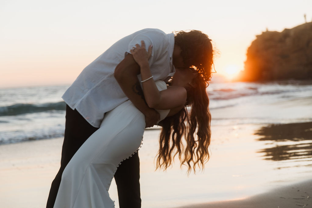 Groom dipping the bride for a kiss at sunset on the beach