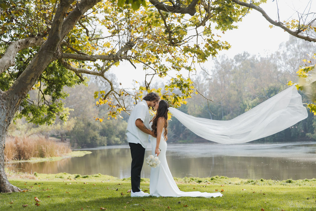 Bride's cathedral veil streaming beside a lake at the first look