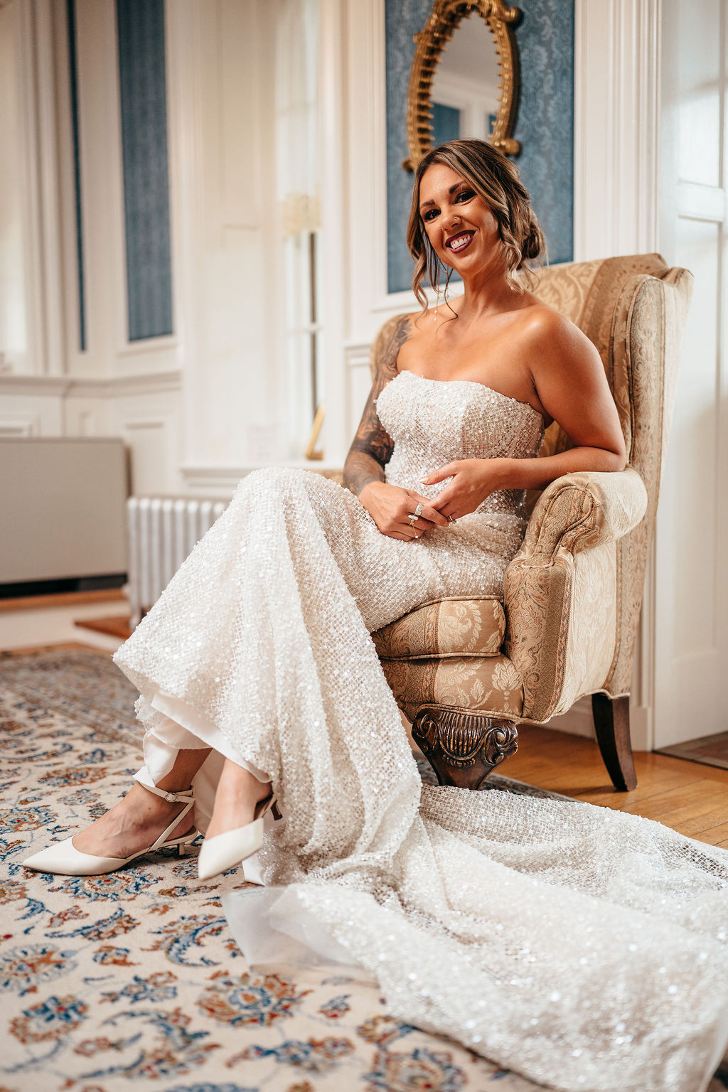 Kristin smiling in her beaded gown on an ornate chair while getting ready
