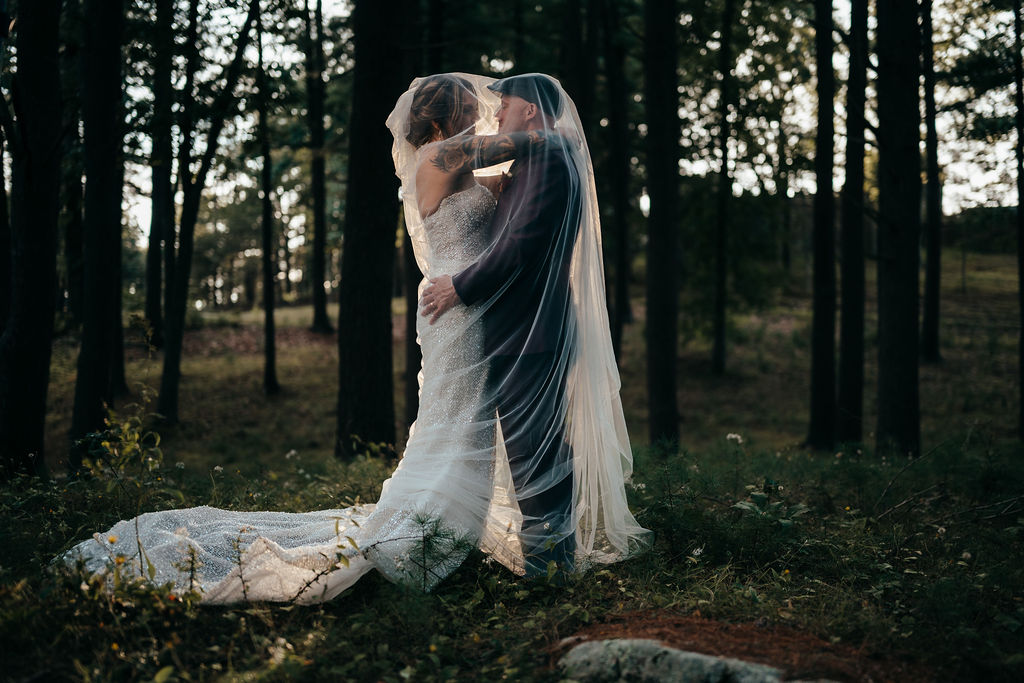 Kristin and Mike kissing in the woods, her veil flowing over both of them