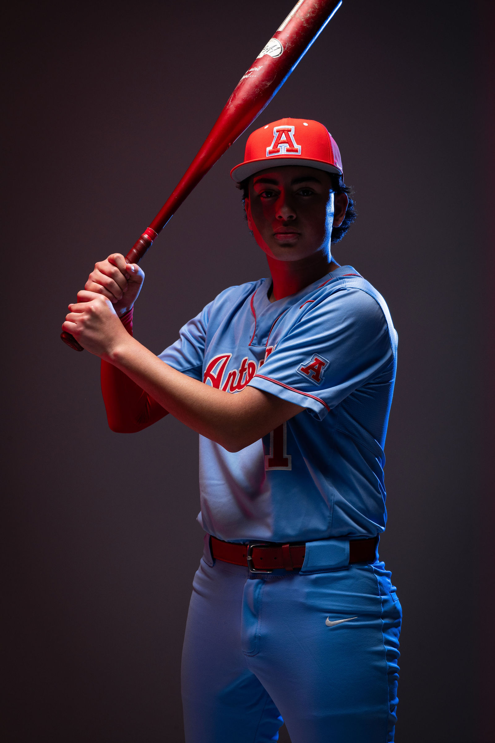 Antonian baseball athlete posing with a bat under red and blue media day lighting