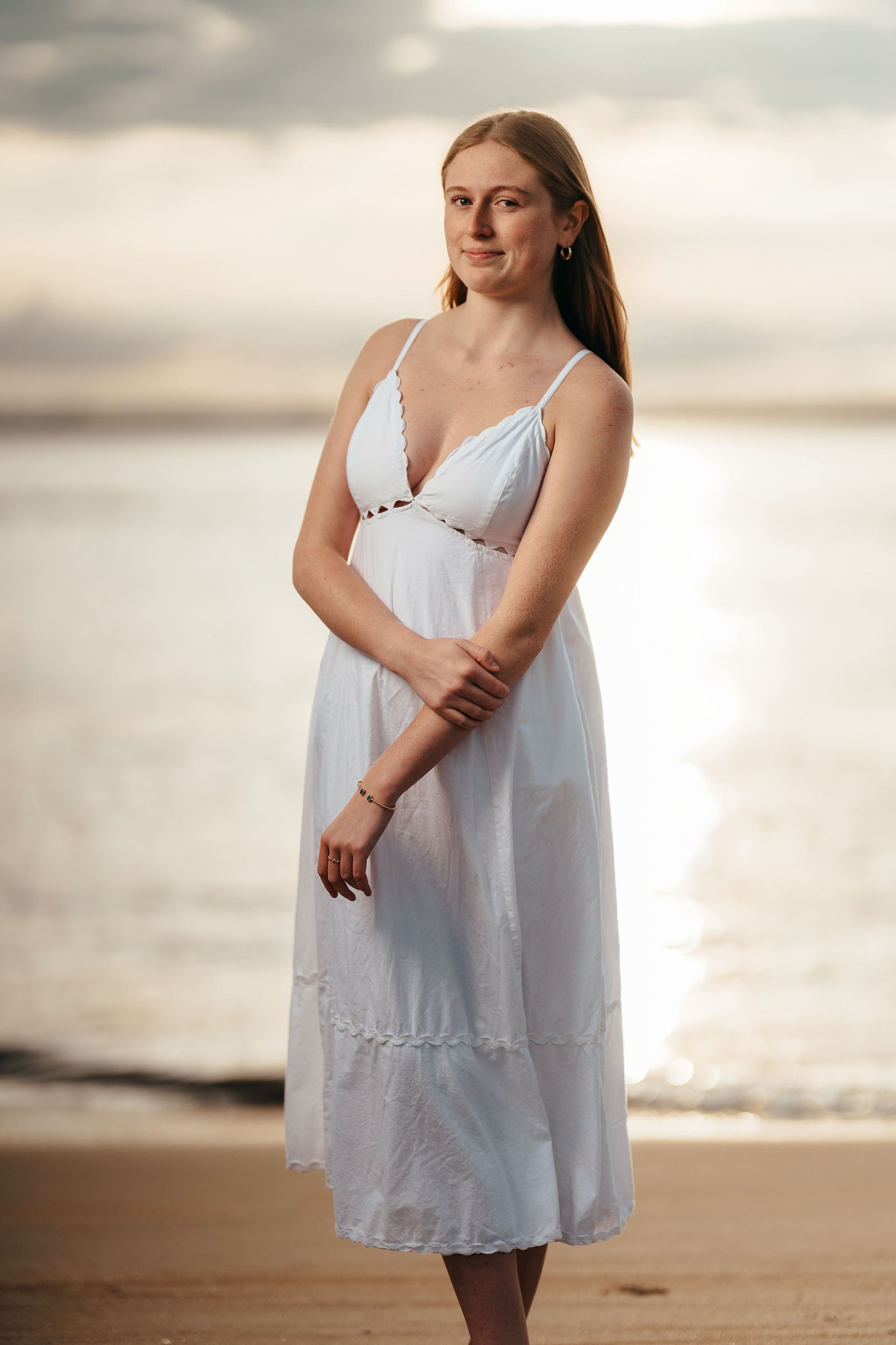 Arianna on the beach at sunset in a white dress during her senior portrait session