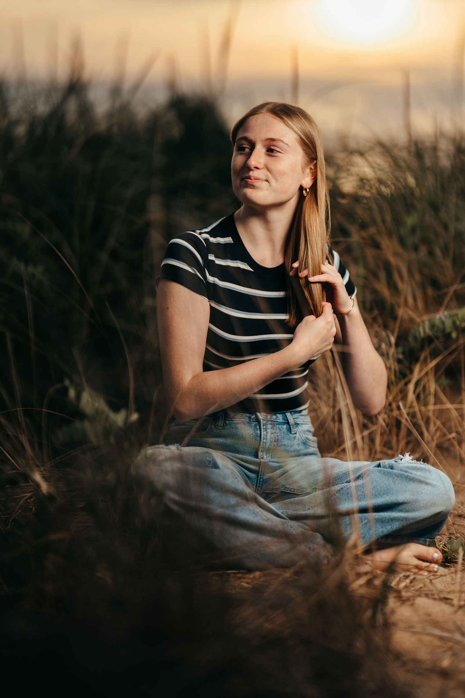Arianna sitting in the dunes at sunset during her senior portrait session