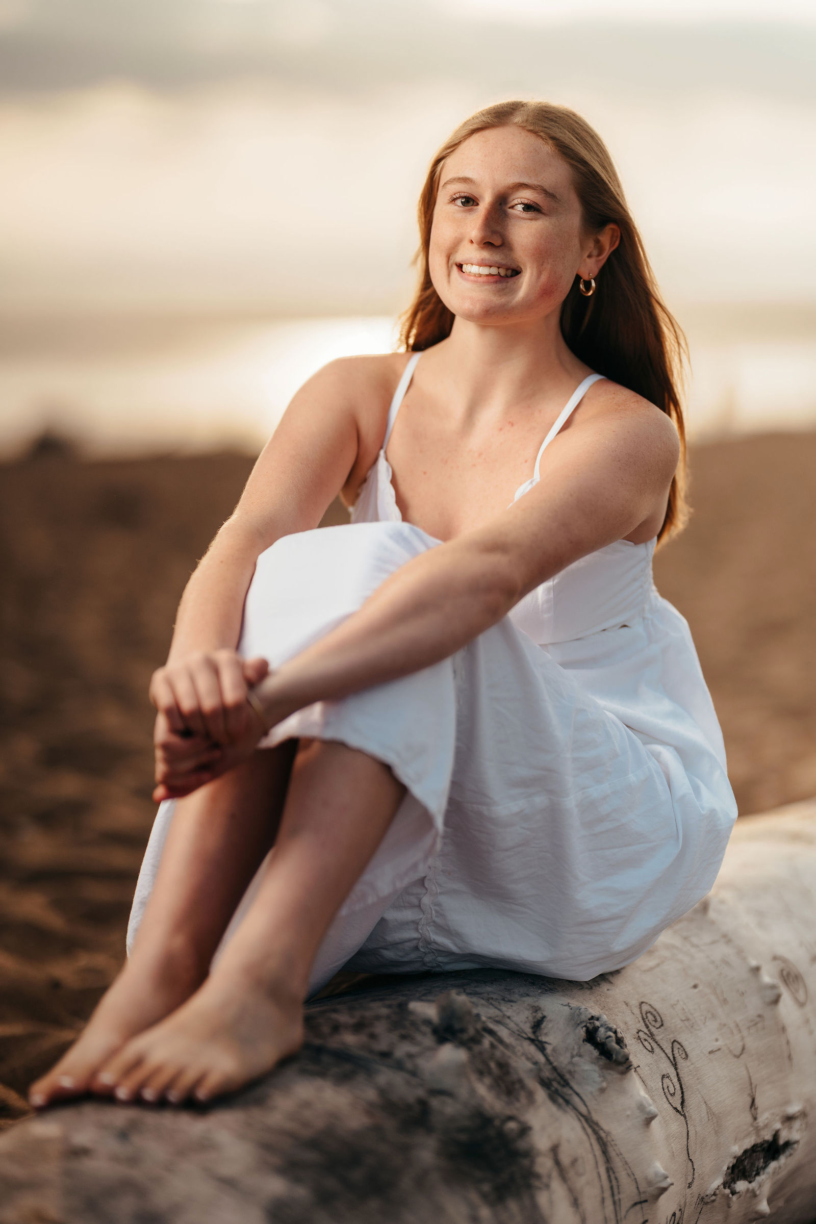 Arianna sitting on driftwood at golden hour during her senior portrait session