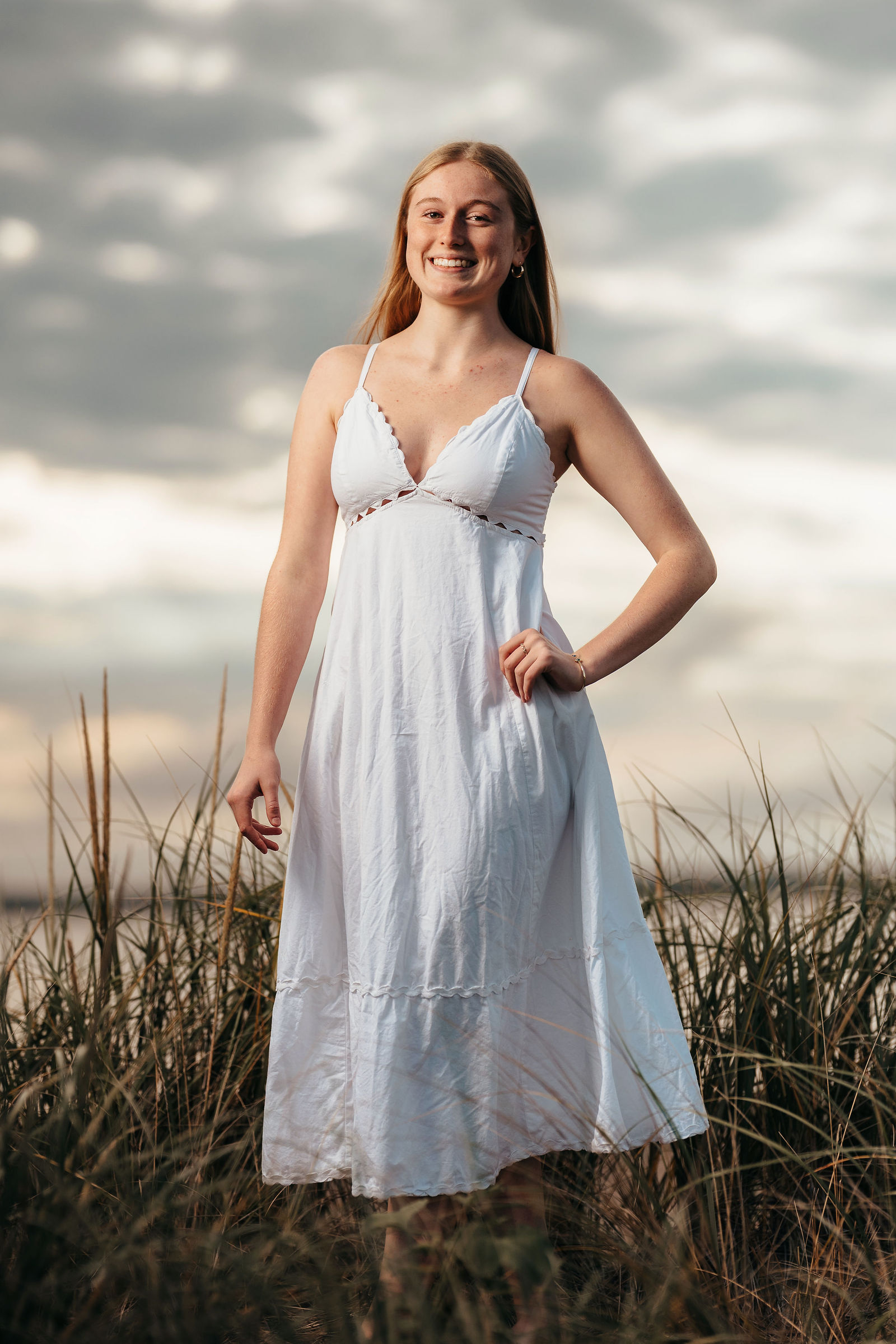 Arianna in a white dress in tall dune grass at the beach during her senior portrait session