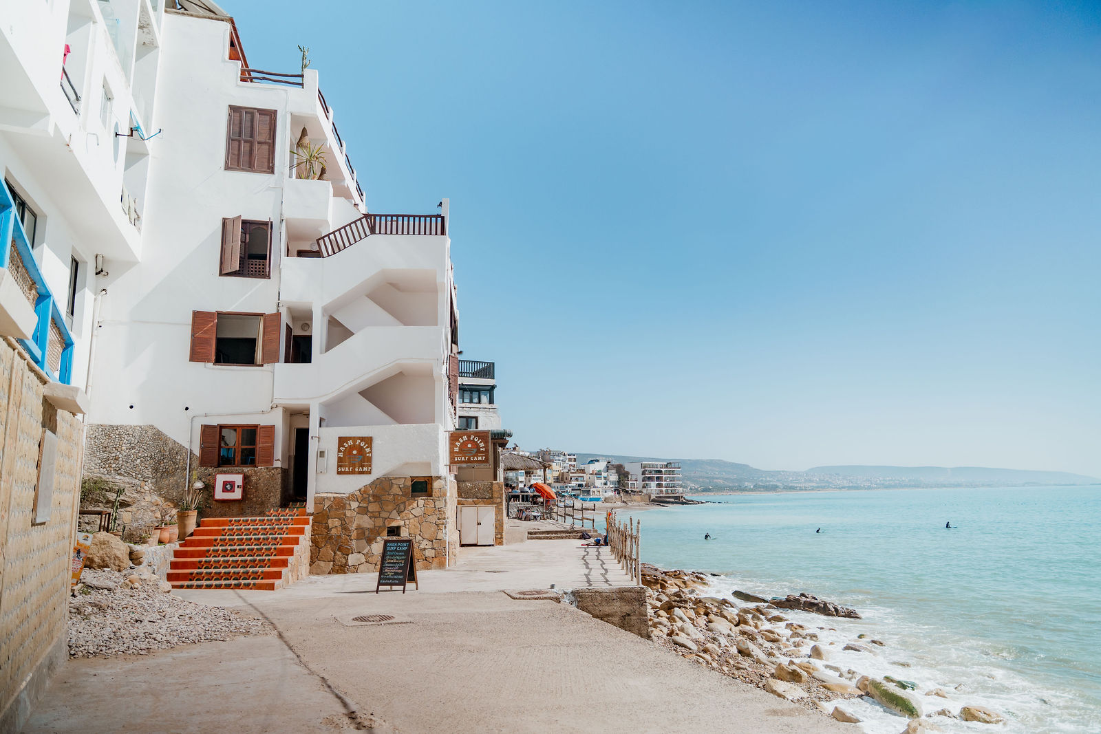 White village buildings and a coastal walkway beside the Atlantic in Taghazout