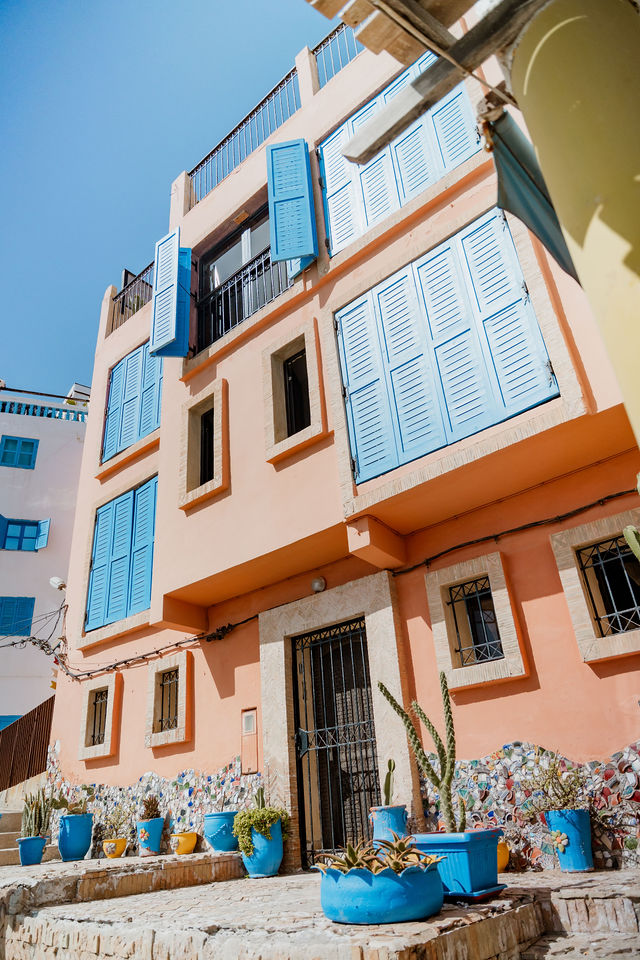 Warm coloured facade with blue shutters and painted plant pots in Taghazout