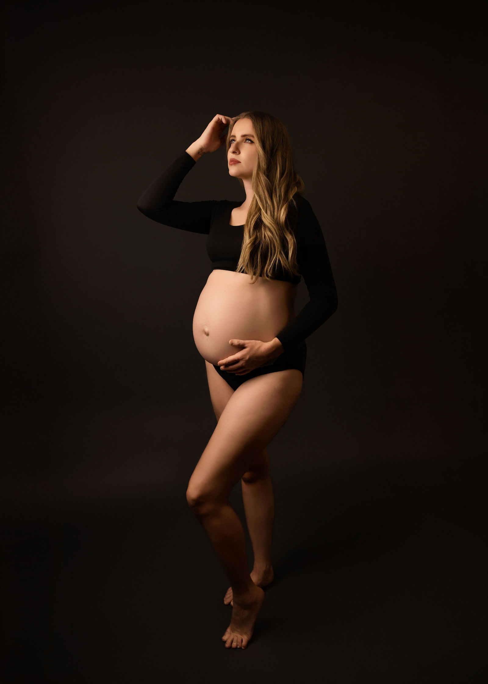 Pregnant woman in a black maternity outfit posed against a dark studio background