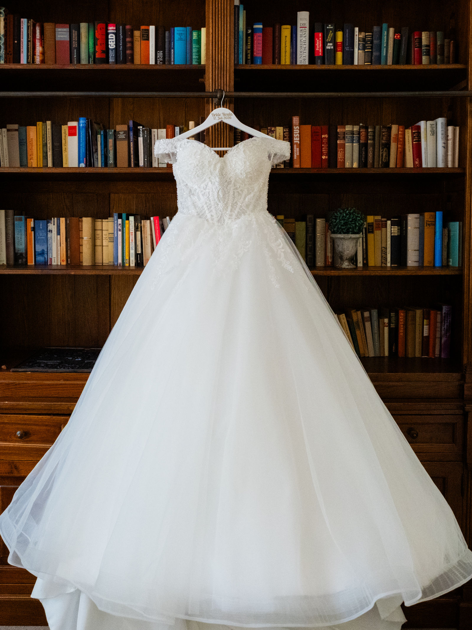 Brautkleid hängt vor einem Bücherregal im Café Wildau, Getting Ready Detailfoto einer Hochzeit in Brandenburg