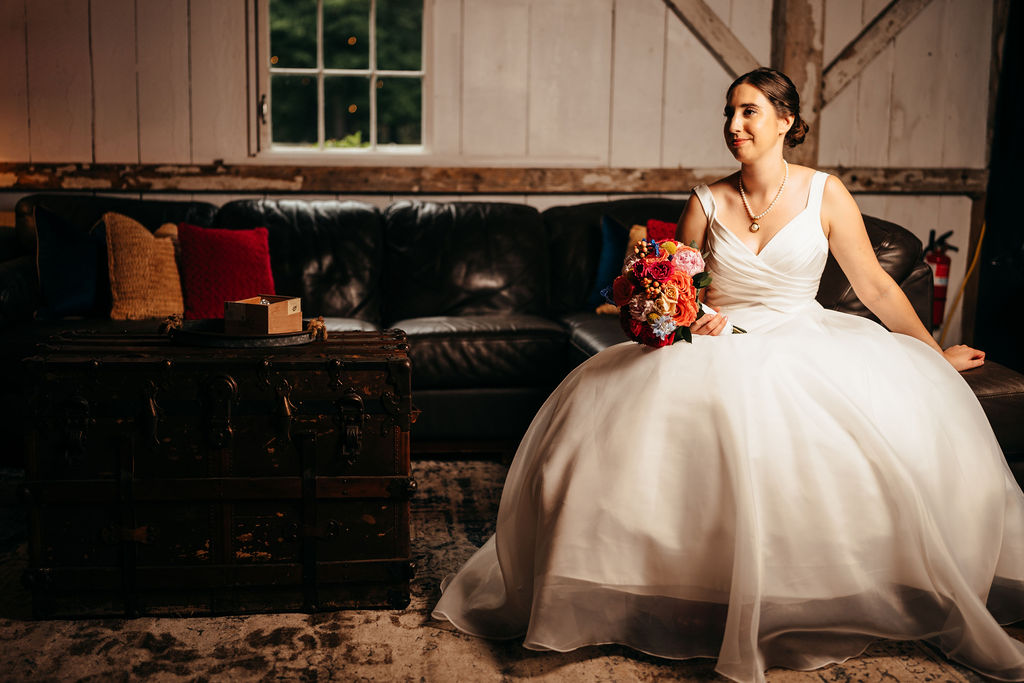 Bride sitting on a couch in the barn holding her bouquet