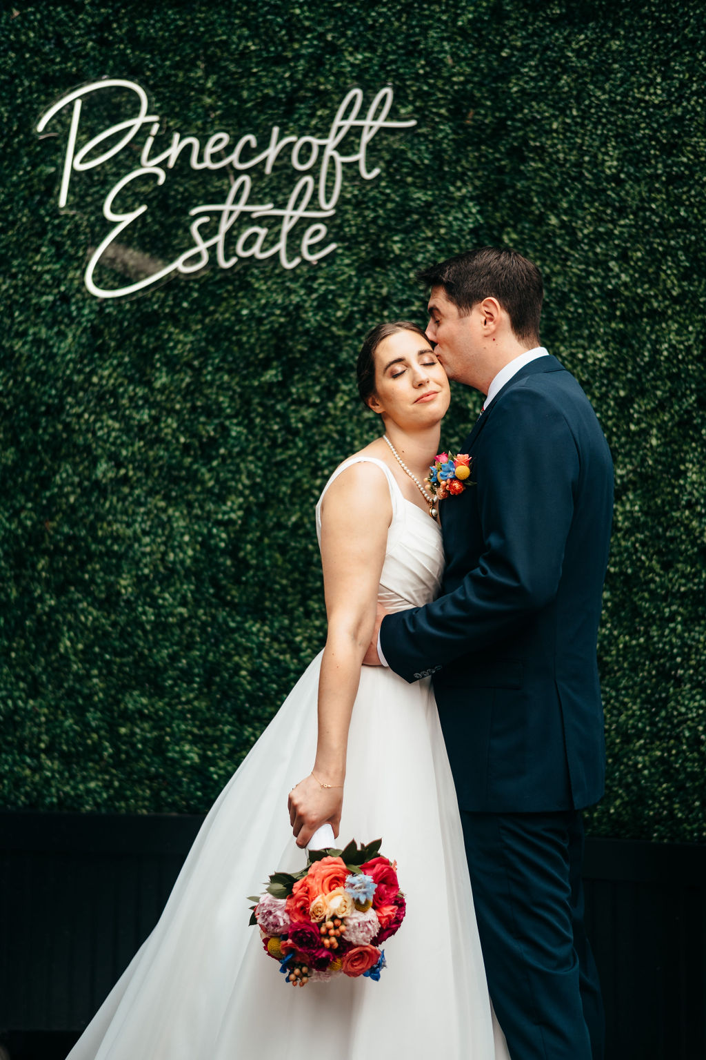 Couple kissing in front of a Pinecroft Estate neon sign