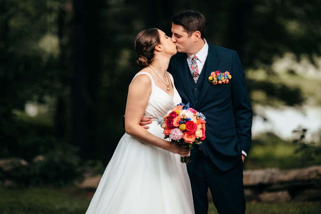 Couple kissing, bride holding a colorful bouquet
