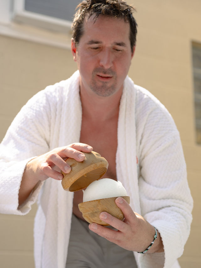 Guest in a terry cloth robe holding a wooden bowl with an aromatherapy snowball inside