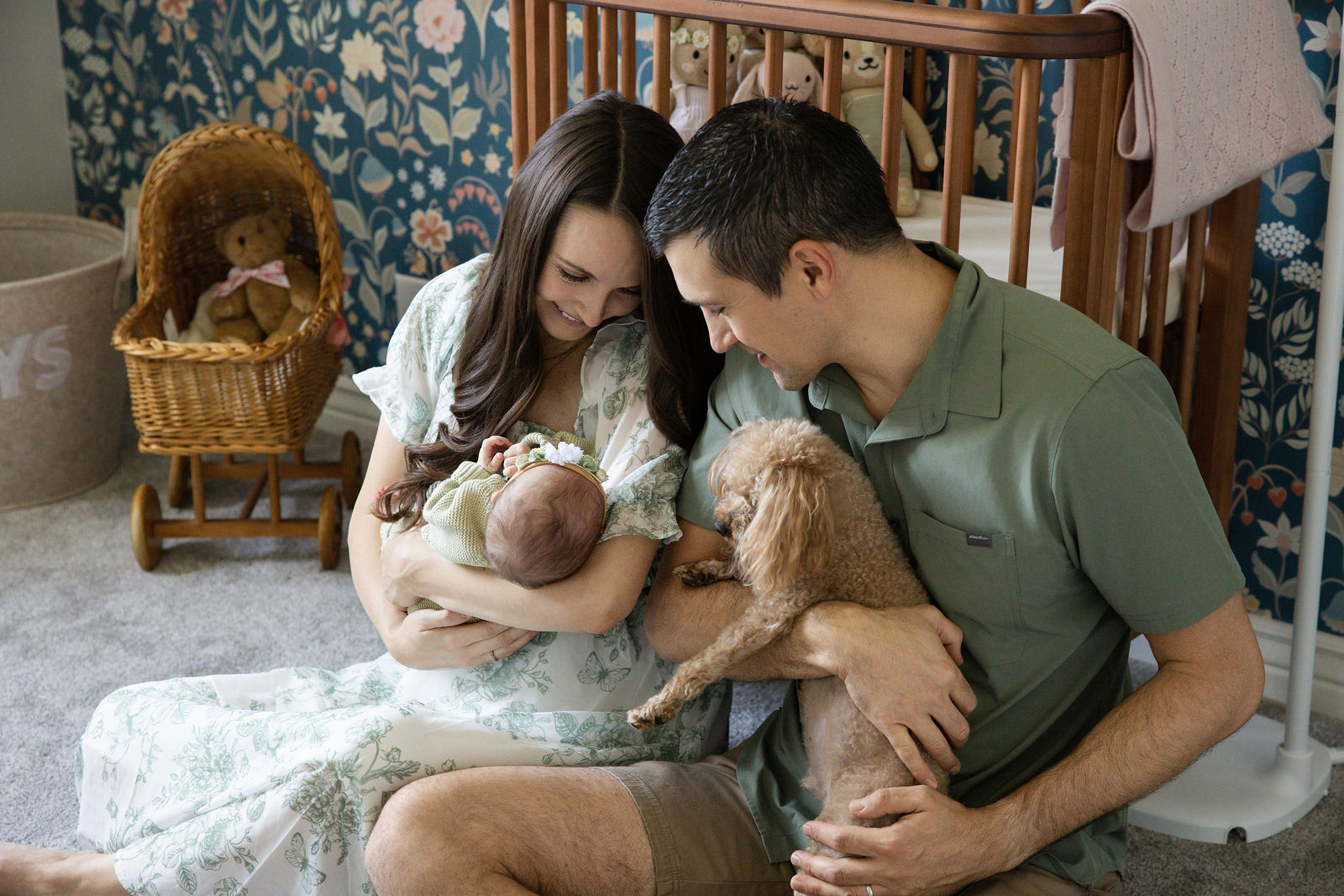 Parents holding their newborn baby with their dog beside them in a colorful nursery during an in-home newborn session