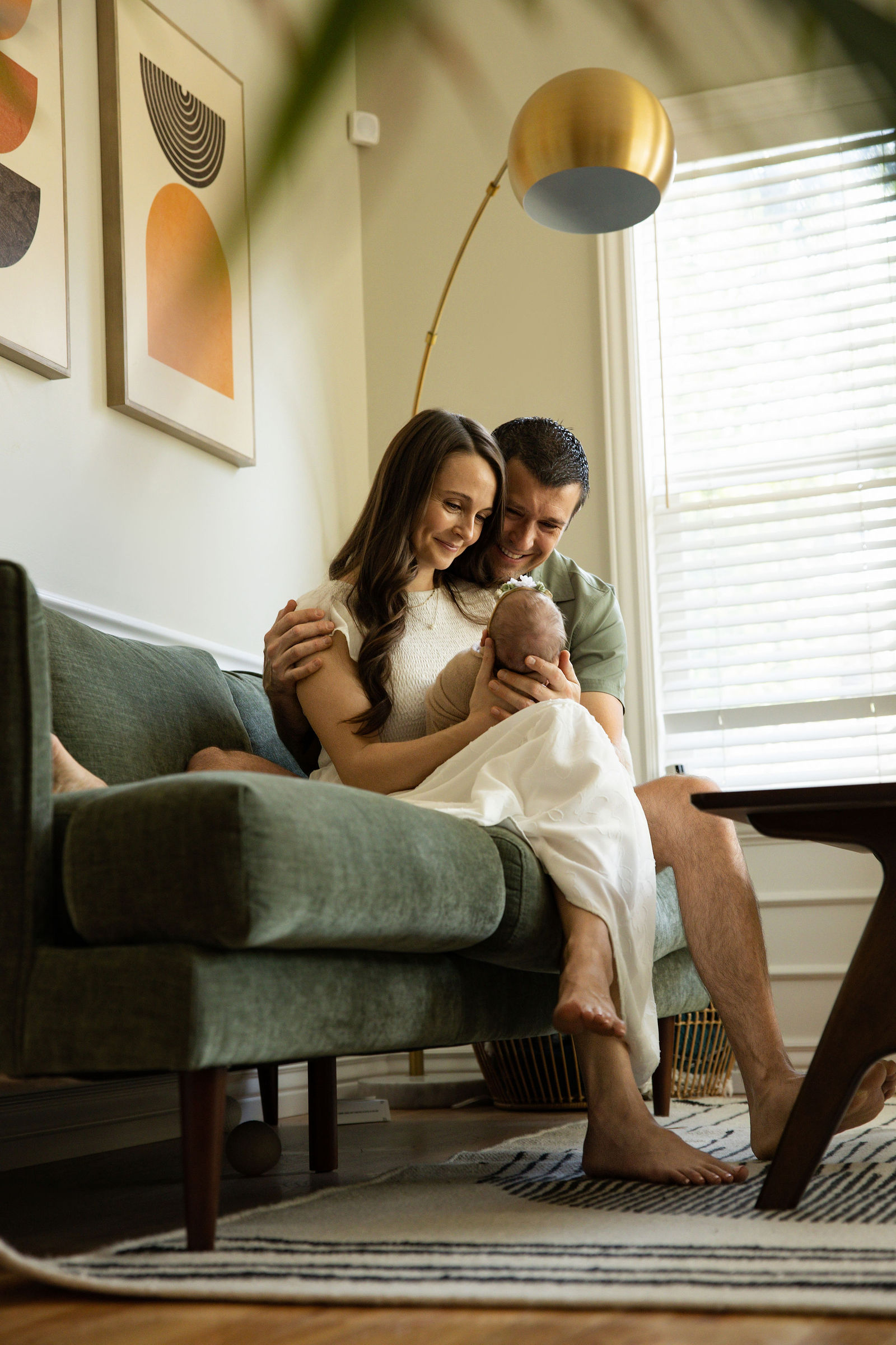 New parents sitting together in a living room chair while cuddling their newborn baby at home