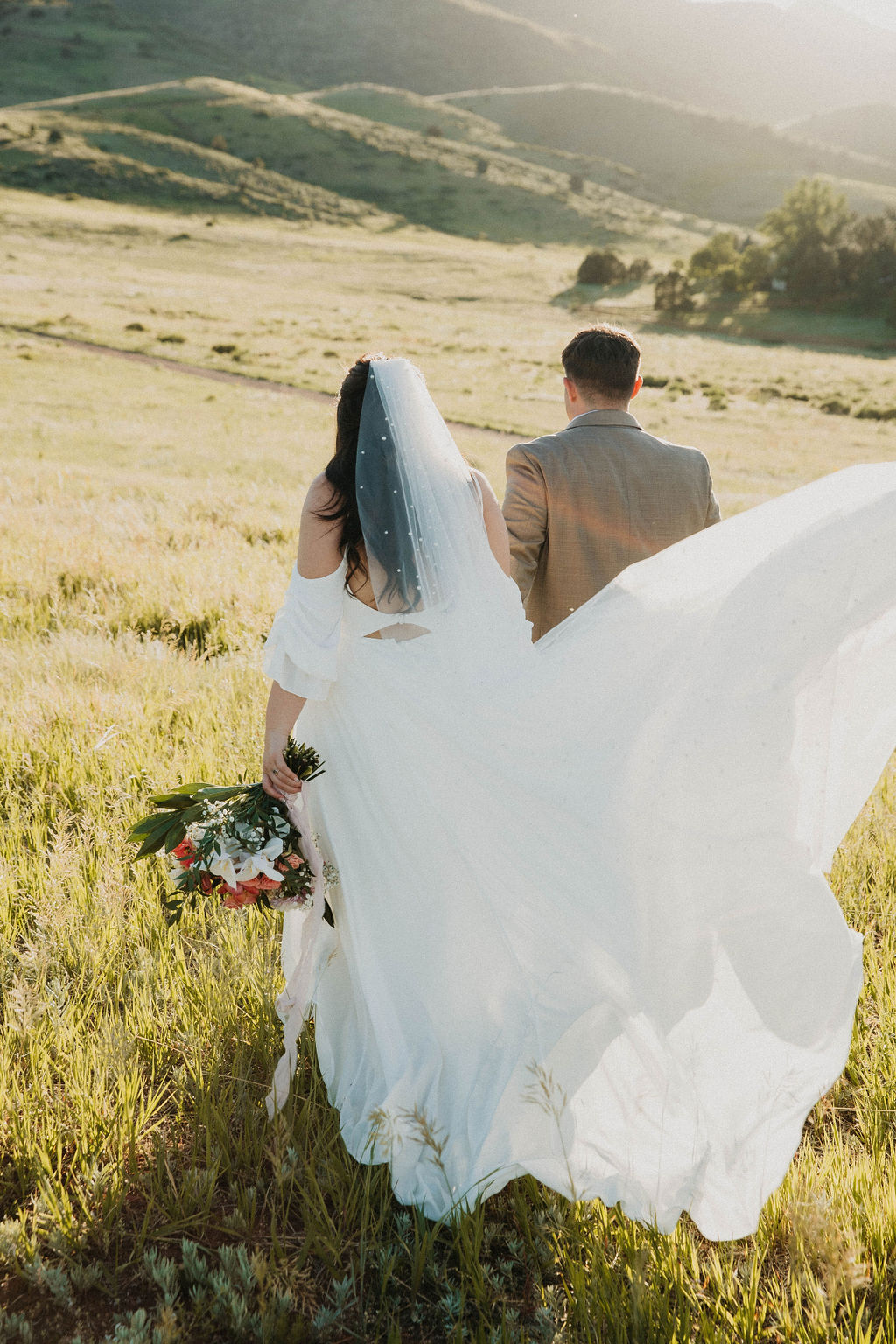 Bride's veil flowing across a golden meadow with mountains behind