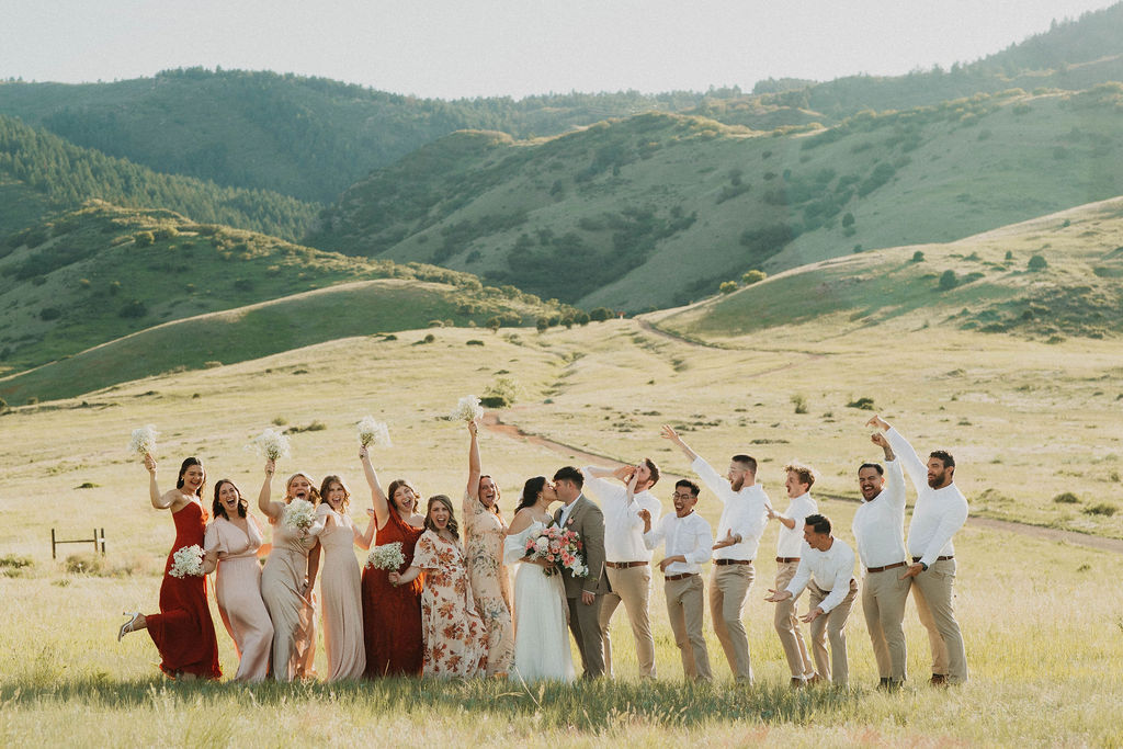 Wedding party cheering in a green meadow with rolling hills