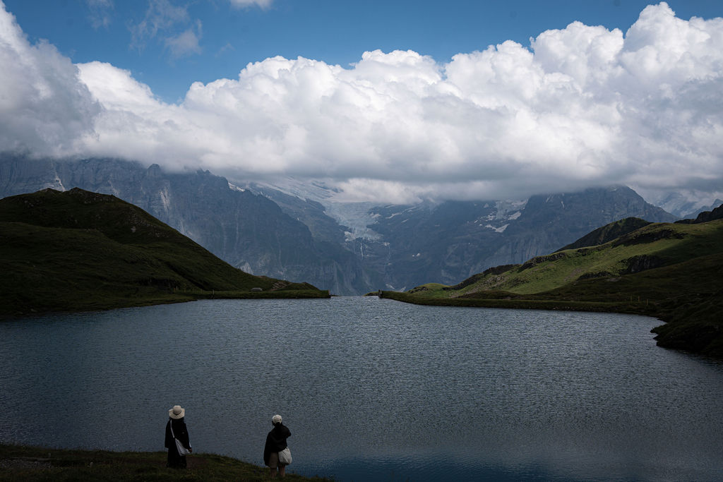 Two hikers by a mountain lake under big clouds, Grindelwald